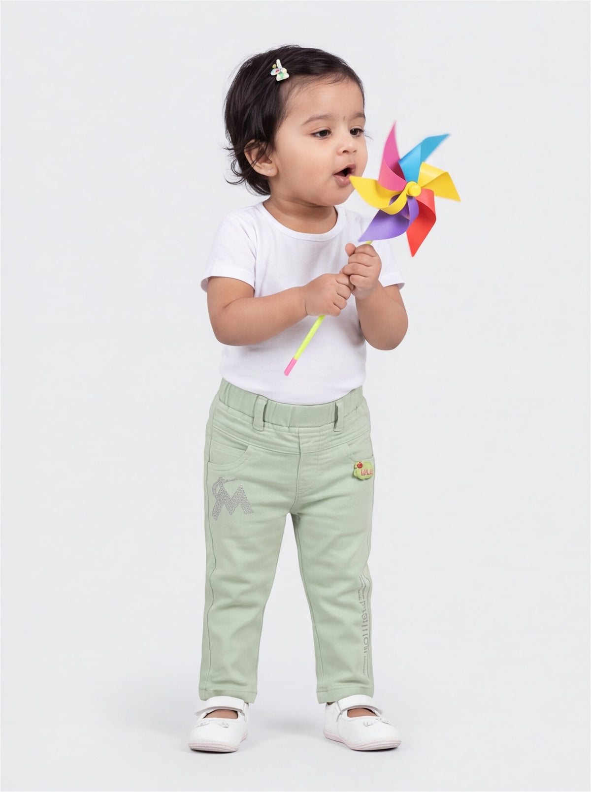 Baby girl in mint green denim pants blowing a pinwheel