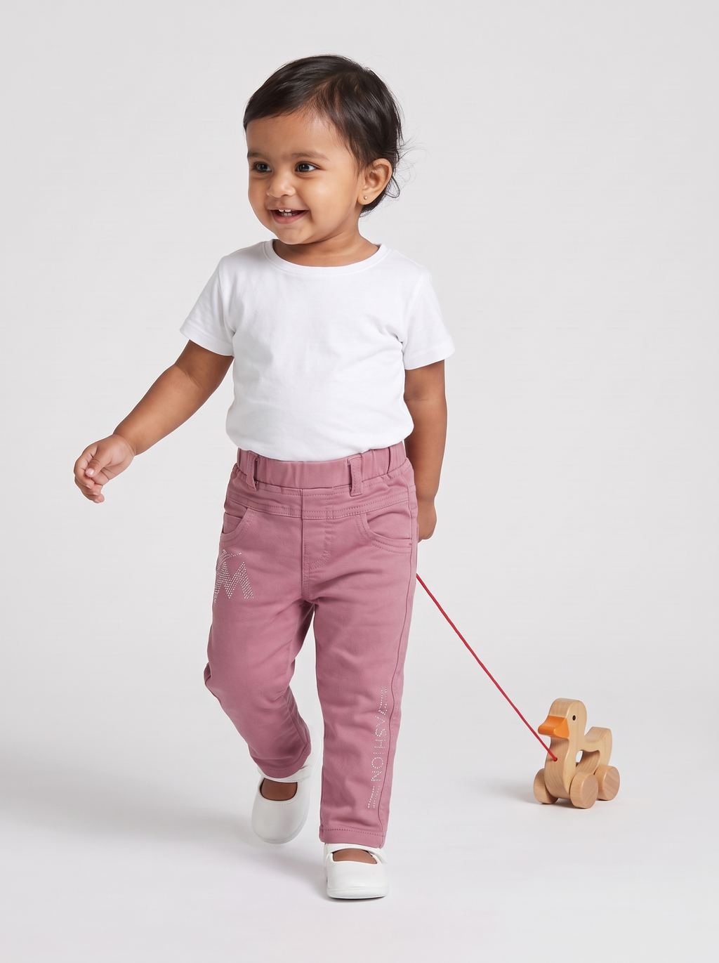 Baby girl in dusty pink denim pants pulling a toy duck