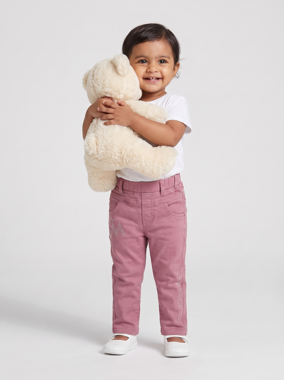 Baby girl in dusty pink denim pants hugging a teddy bear