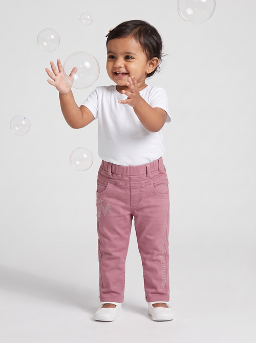 Baby girl in dusty pink cotton denim pants playing with bubbles