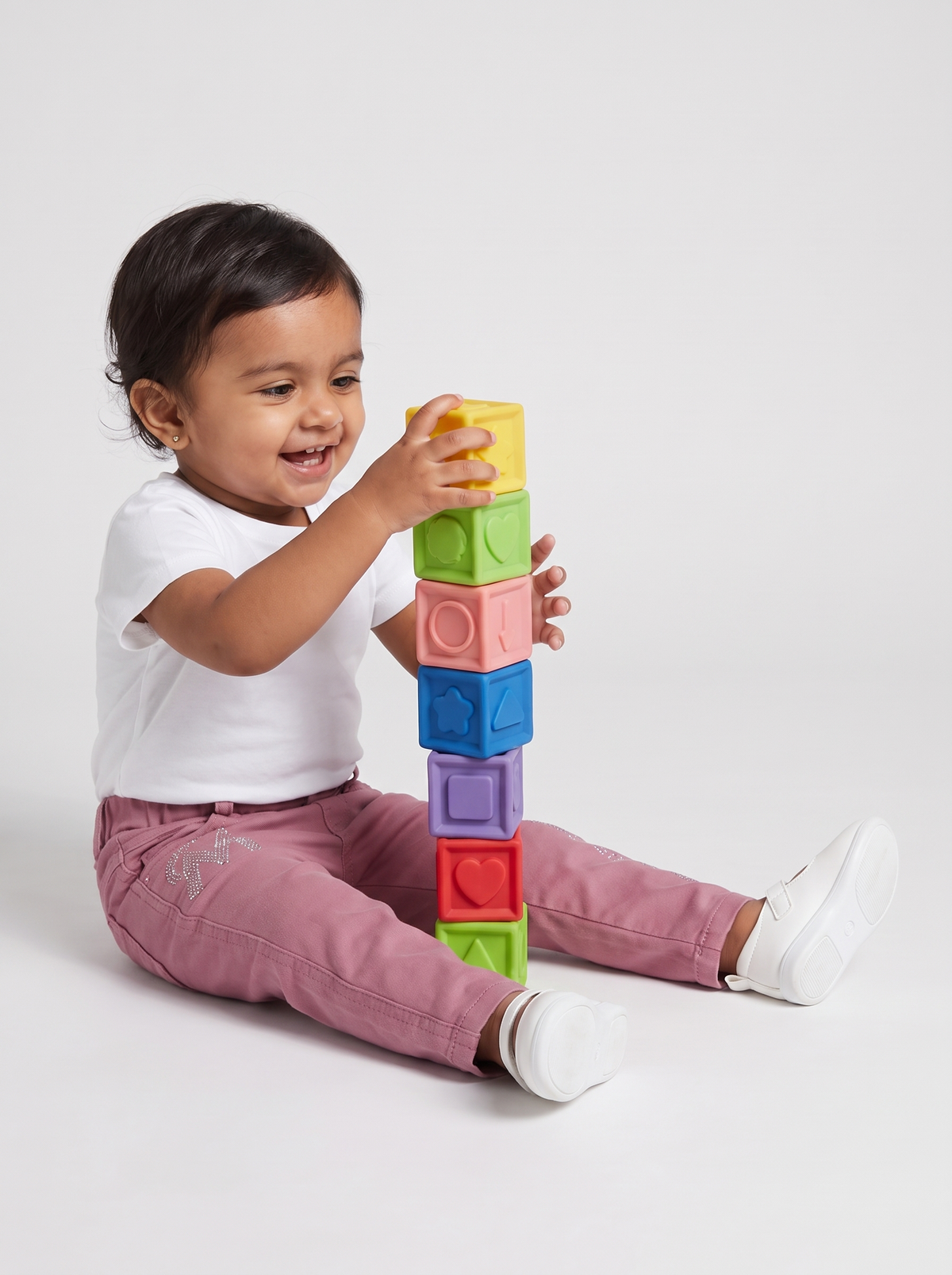 Baby girl in dusty pink denim pants stacking toy blocks