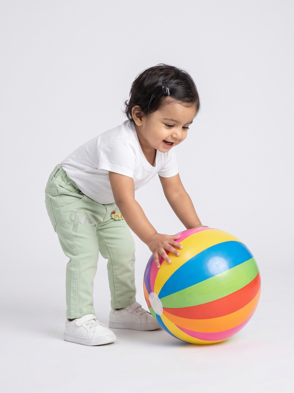 Baby girl in mint green cotton denim pants playing with a big beach ball