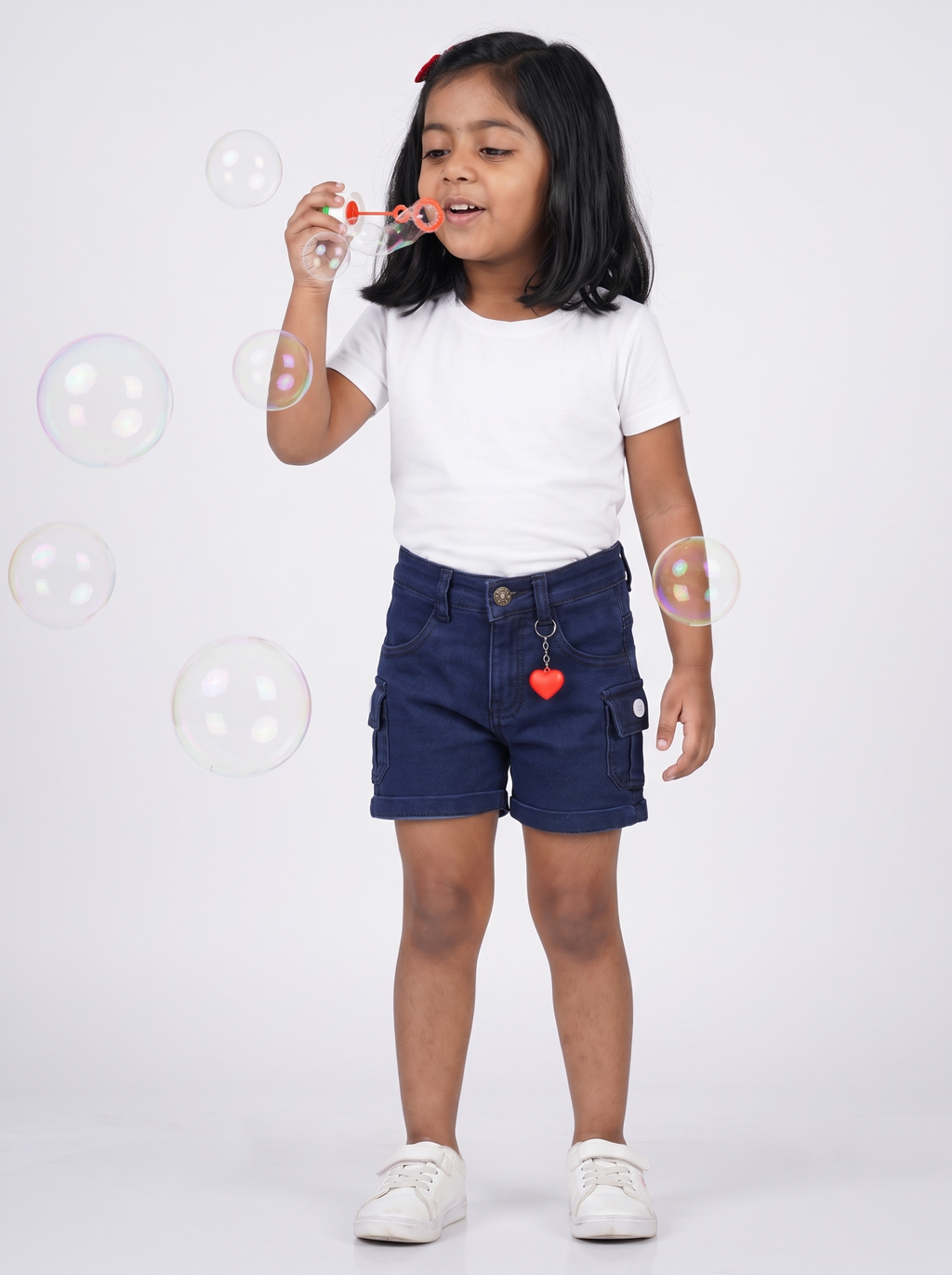 Girl wearing navy denim cargo shorts, blowing bubbles
